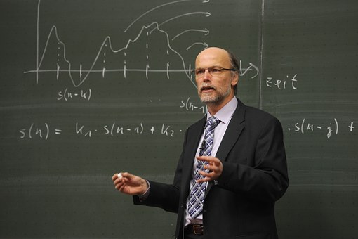 male college teacher lecturing with blackboard at his back