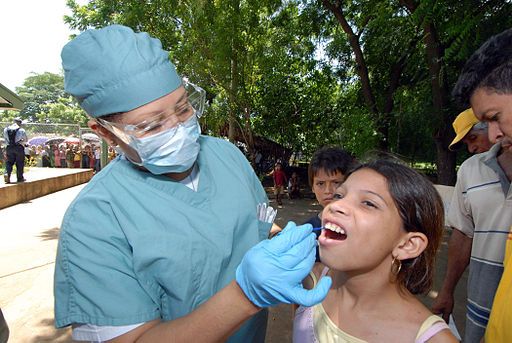 doctor in full medical dress checking out the mouth of a young girl