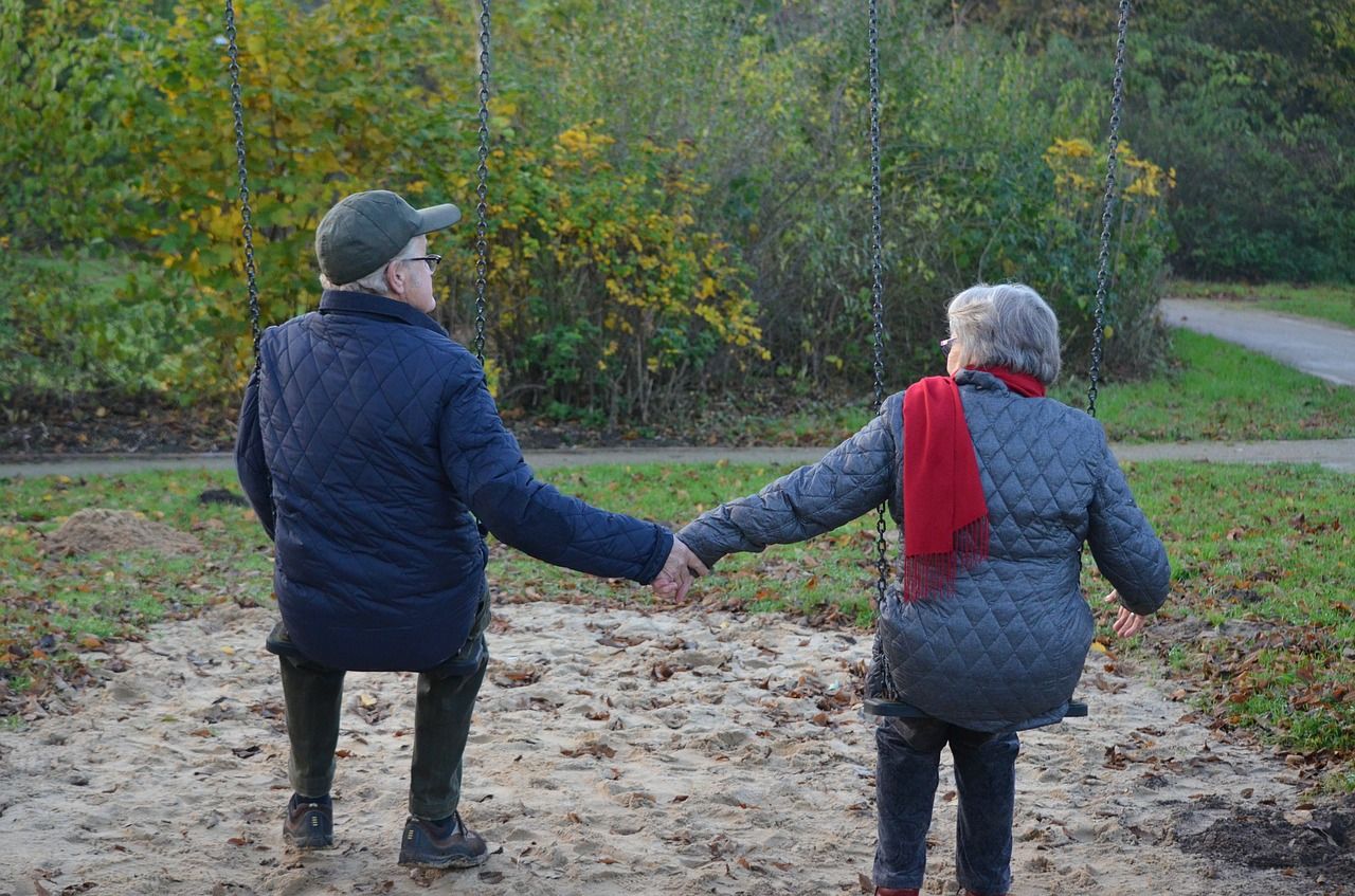 two elders sitting on swinghs and holding hands