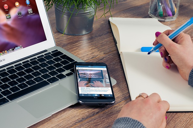 woman taking notes next to computer and cellphone