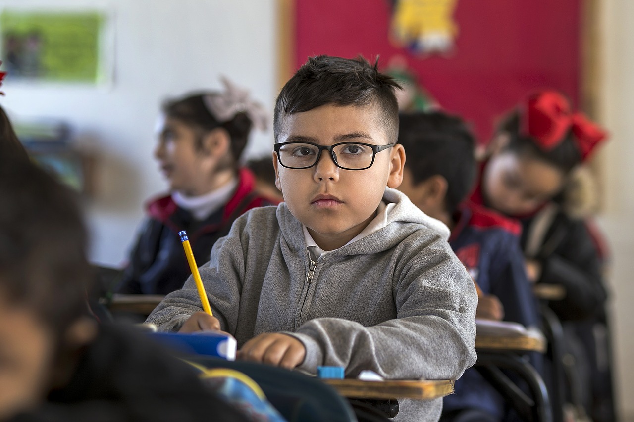 child looking at camera in classroom while other students work at desks