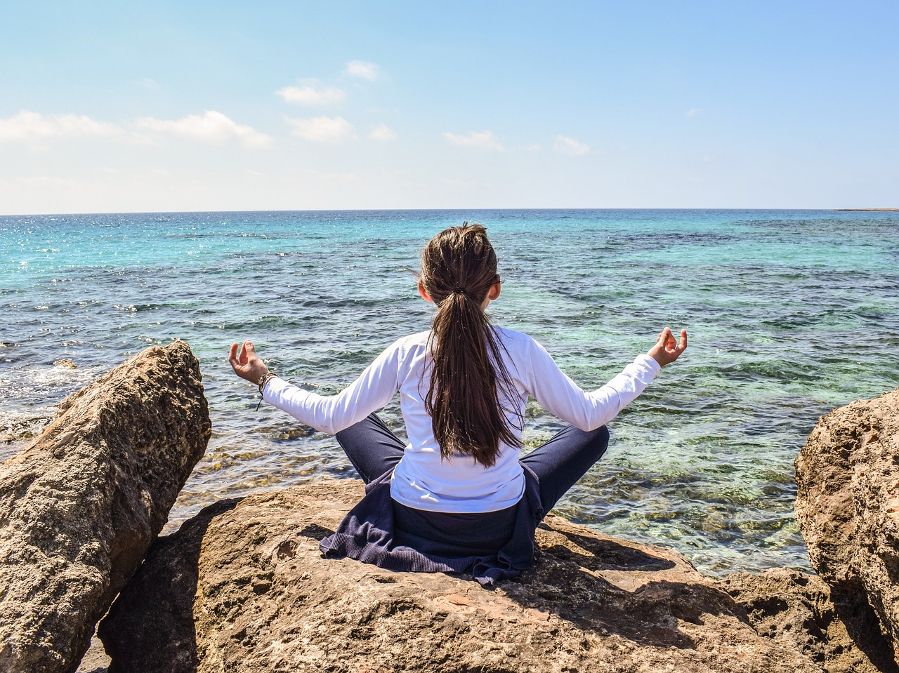 girl with legs crossed and arms out looking out at ocean