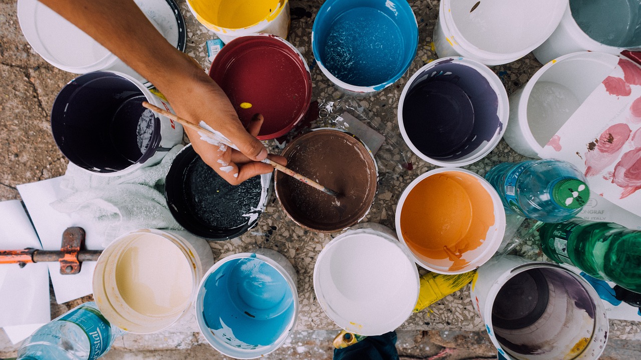 cups of colored paint and person with paintbrush dipping into brown paint